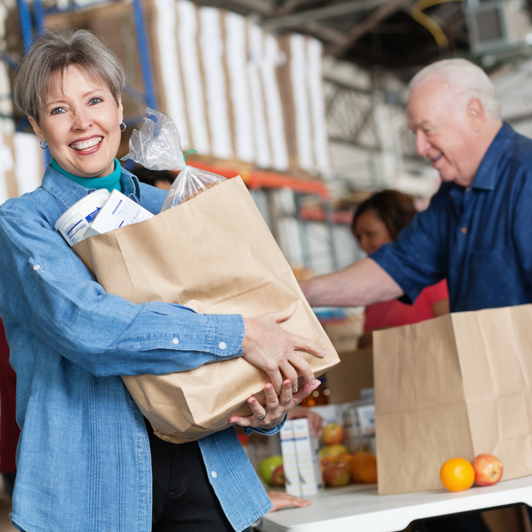 Hands holding grocery bag filled with nonperishable food and fresh produce, symbolizing community giving.